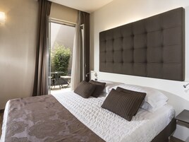 Habitación de hotel con una cama grande, cabecera, mesita de noche y vistas a un patio exterior.