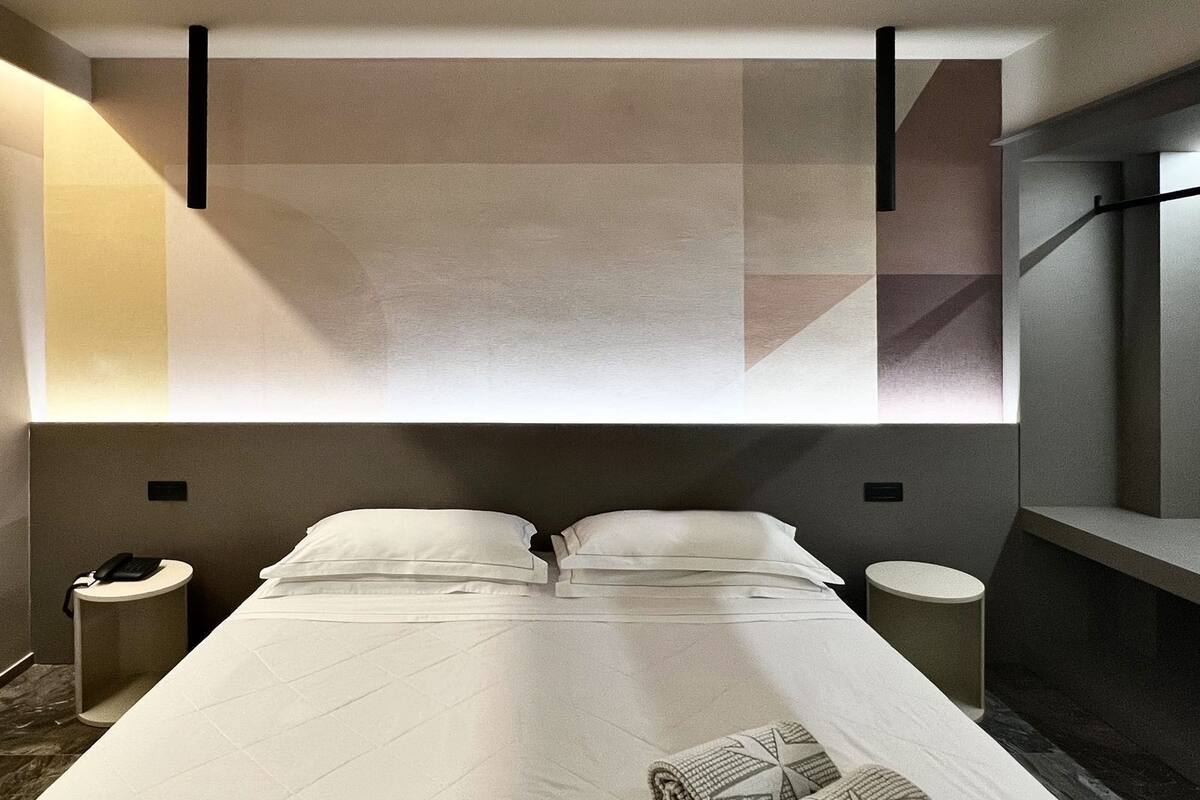 Quarto de hotel moderno com uma cama grande, duas mesas de cabeceira e uma parede com padrão geométrico.