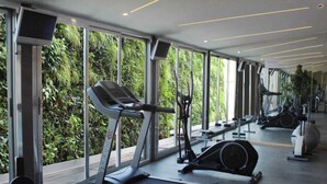 A gym with treadmills, stationary bikes, and weight machines, large windows with a view of greenery.