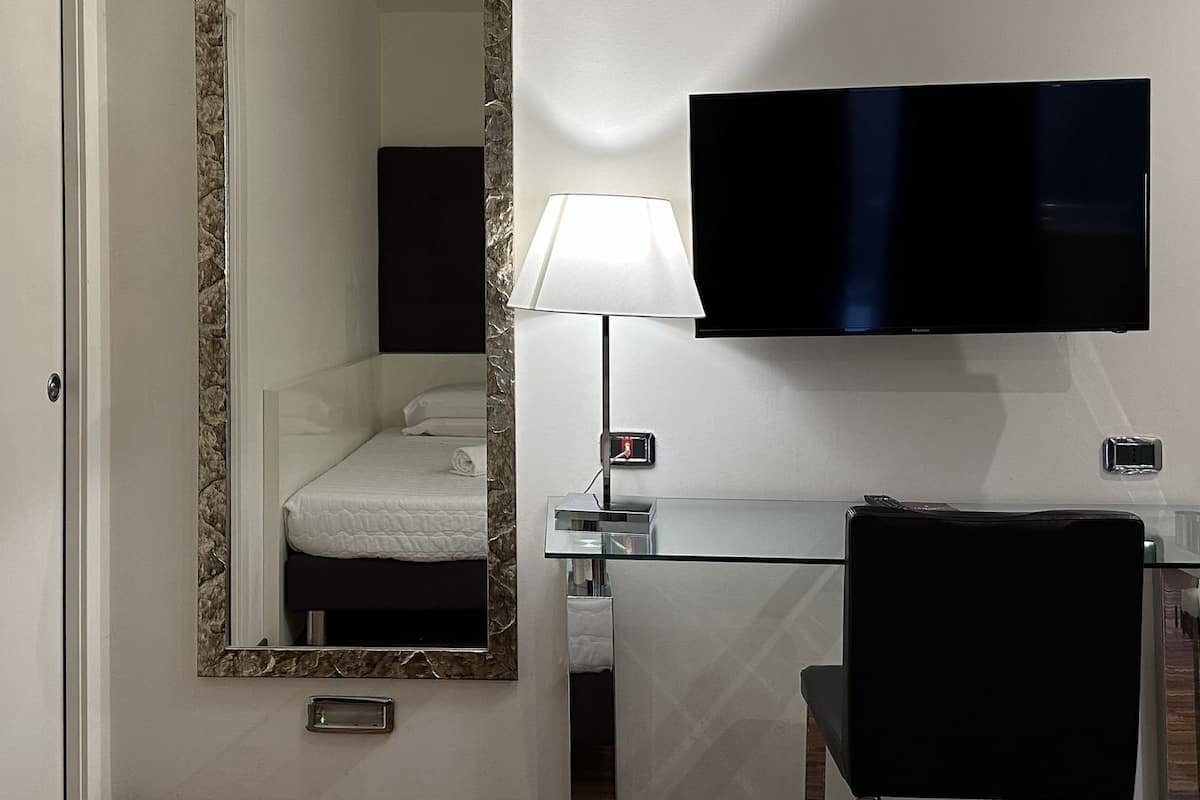 Quarto de hotel com uma cama, uma mesa com luminária, uma televisão e um espelho.