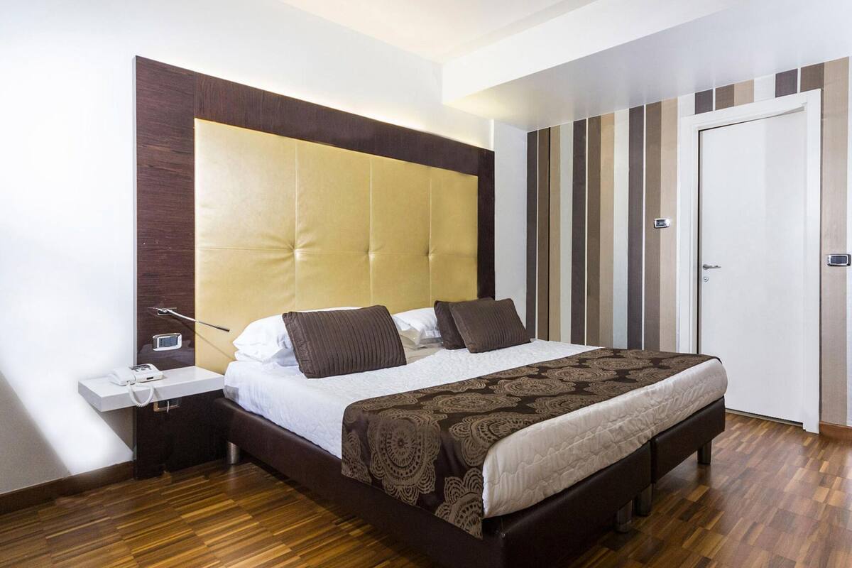 Quarto moderno com uma cama grande, mesa de cabeceira com telefone e guarda-roupa com padrão listrado vertical.