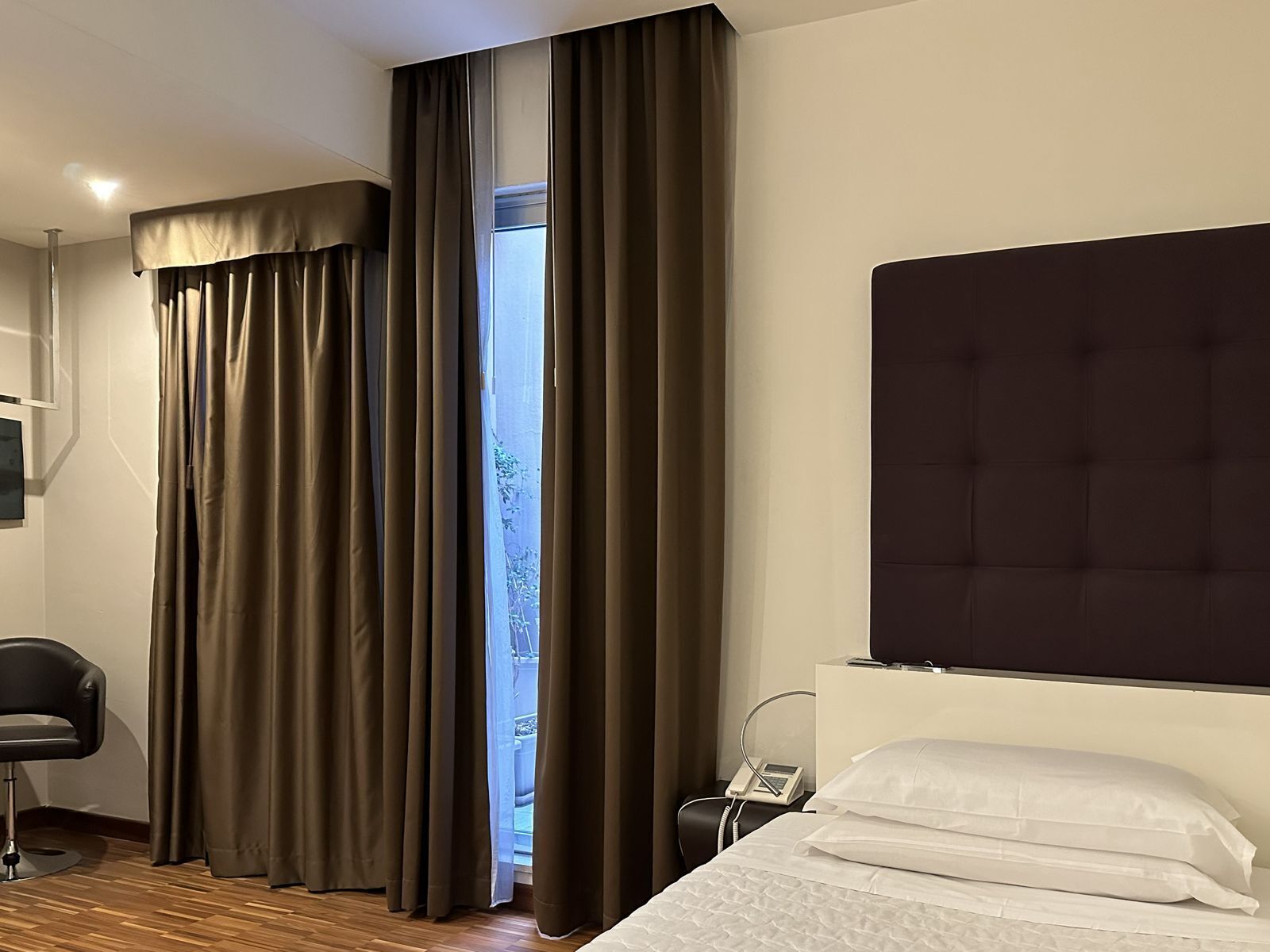 A hotel room with a bed, a bedside telephone, and a chair.