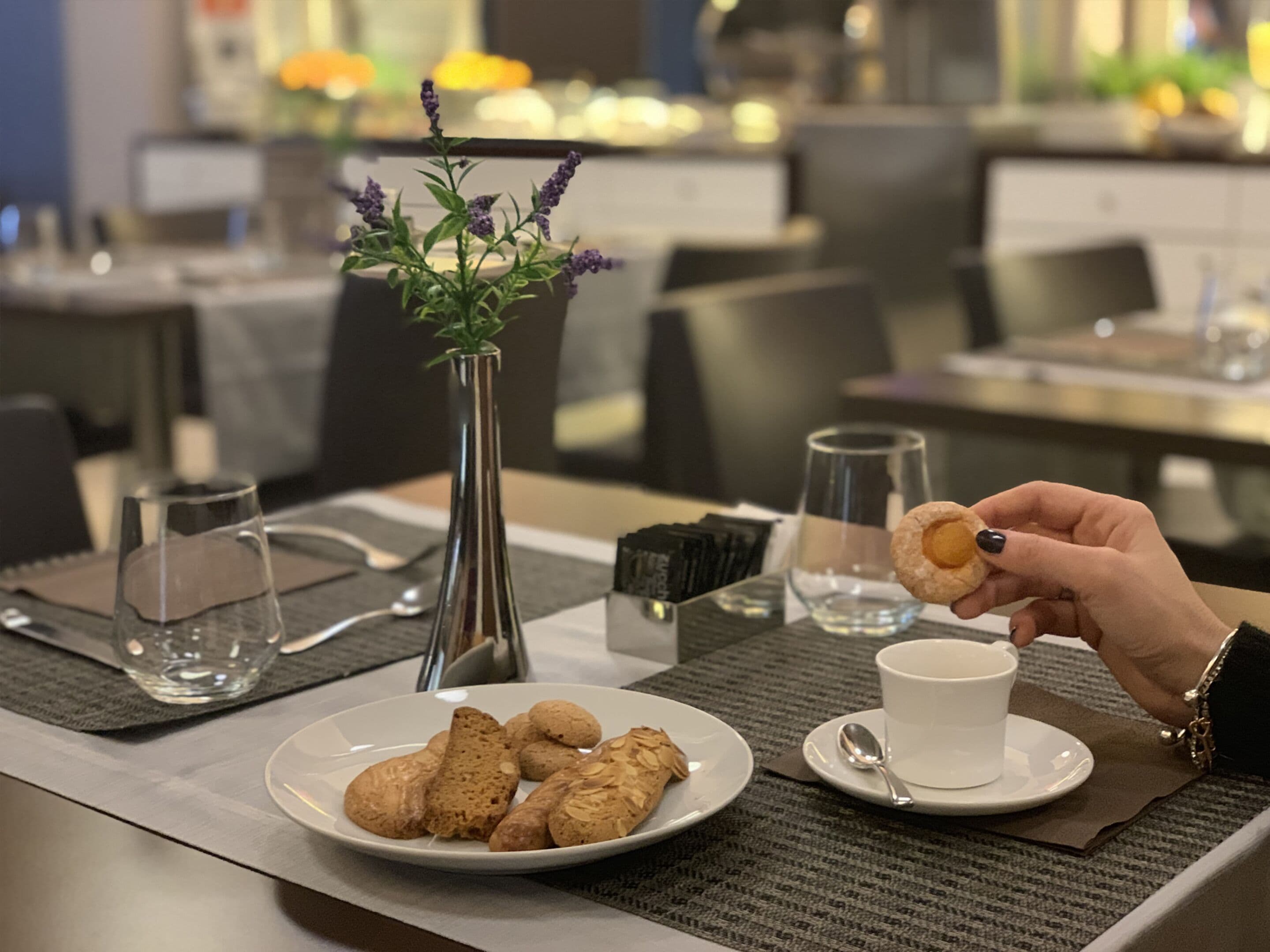 Un tavolo da pranzo con un piatto di biscotti, una tazza di caffè, un vaso con fiori e un bicchiere d'acqua.