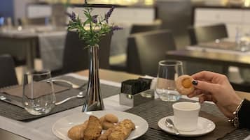Un tavolo da pranzo con un piatto di biscotti, una tazza di caffè, un vaso con fiori e un bicchiere d'acqua.