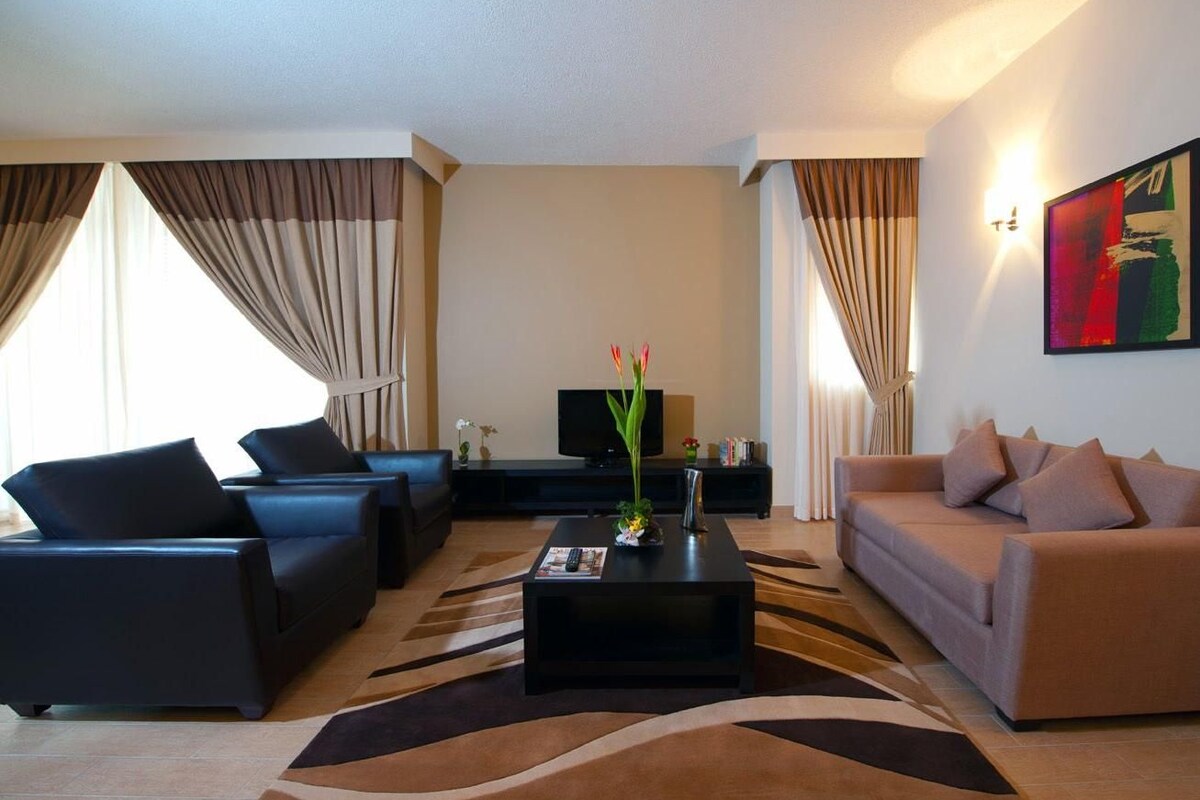A modern living room with a black coffee table, two sofas, a flat-screen TV, and a decorative vase with flowers.