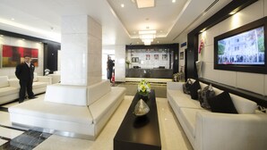 A modern lobby with a reception desk, white sofas, a coffee table with a vase, and a TV screen. - The Apartments Dubai World Trade Centre (Dubai)