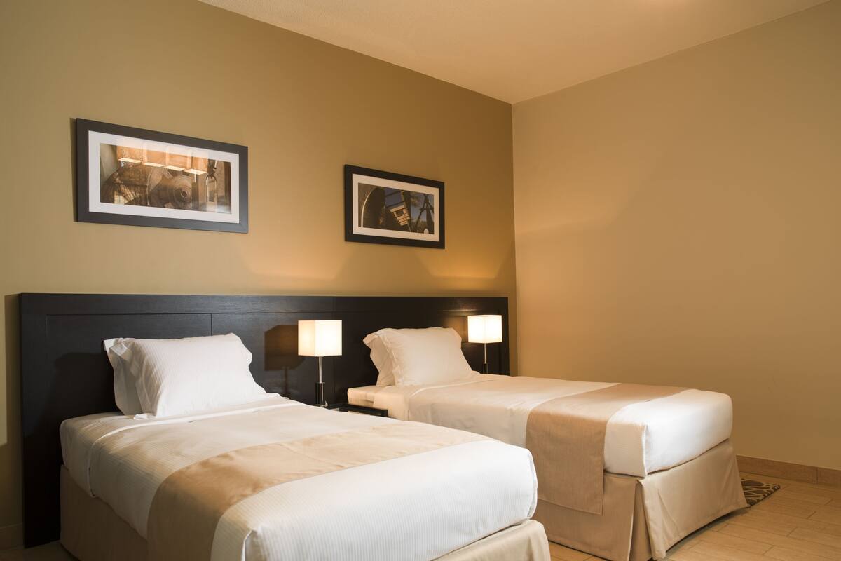 A hotel room with two beds, a dark headboard, and two wall-mounted lamps.