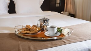 A neatly made bed with white linens, a tray with croissants, a cup of coffee, and a small bouquet of white flowers on a hotel room. - The Apartments Dubai World Trade Centre (Dubai)