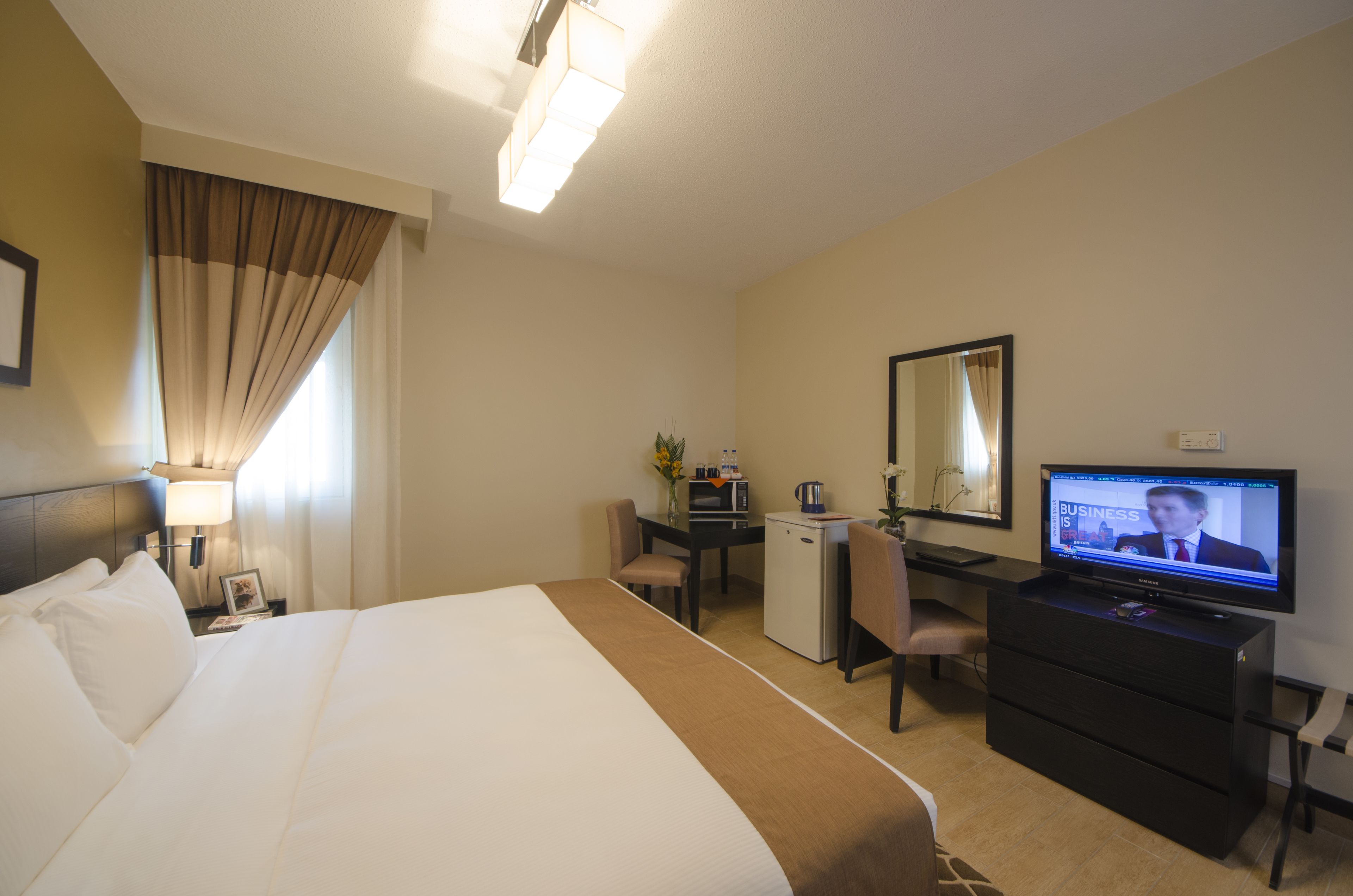 A hotel room with a bed, desk, television, and a small refrigerator.
