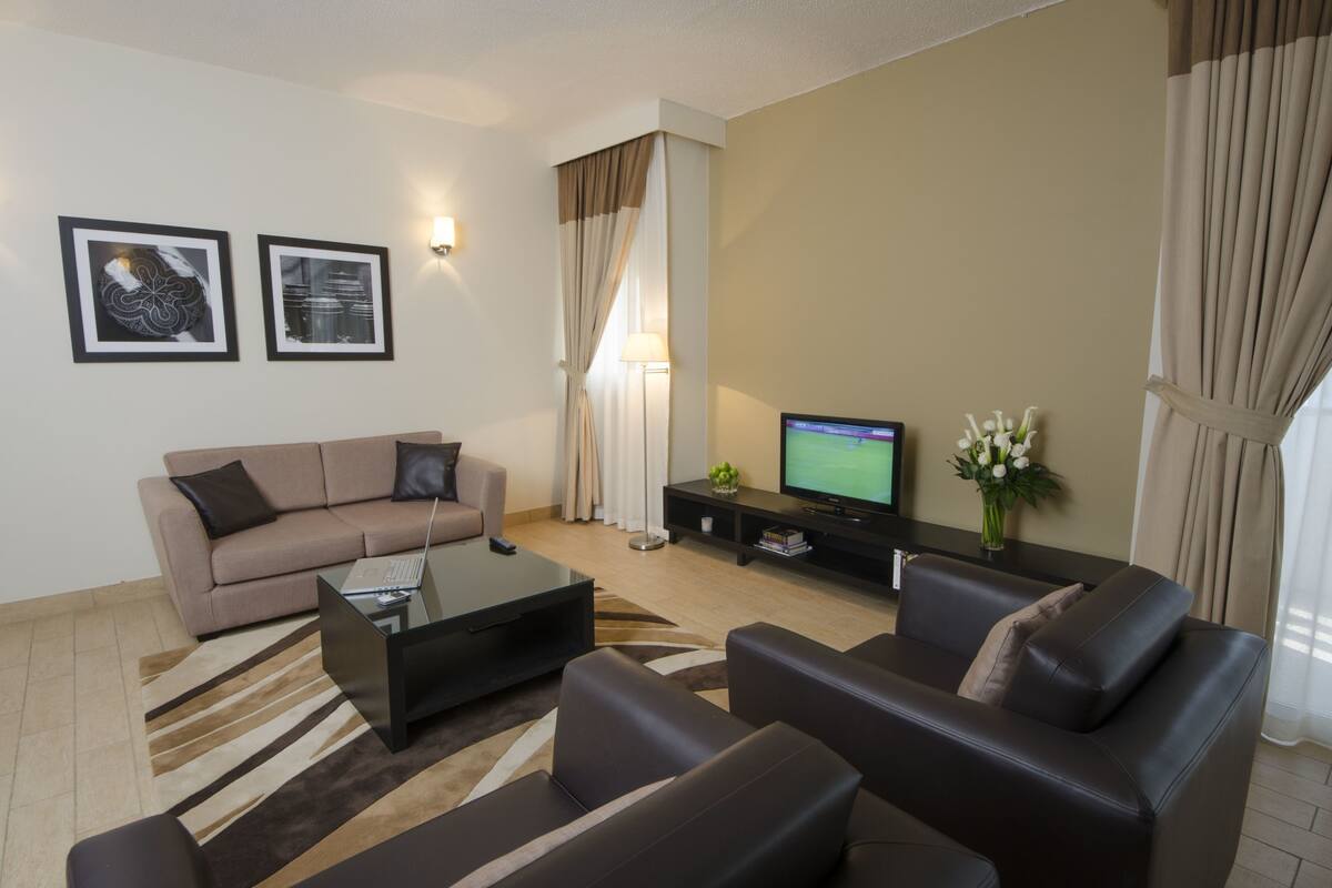 A modern living room with a sofa, coffee table, and TV. There are framed pictures on the wall and a vase with flowers on a side table.