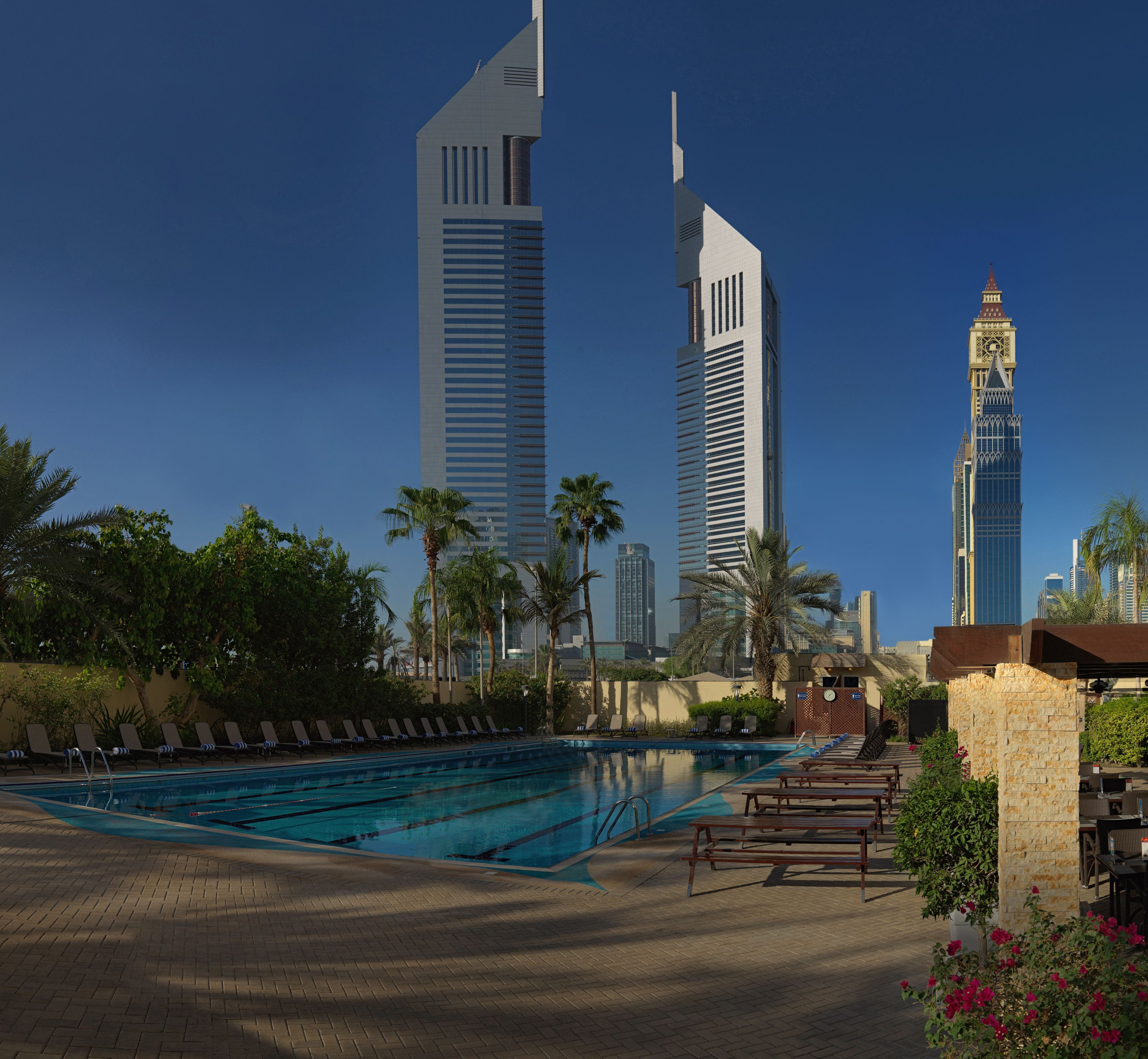 A swimming pool with lounge chairs and palm trees, surrounded by modern high-rise buildings.