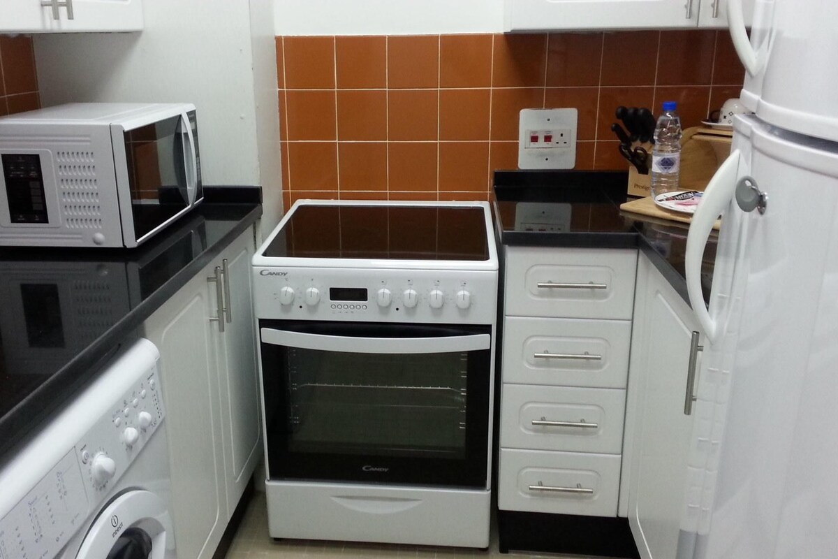 A compact kitchen with a microwave, oven, and washing machine.