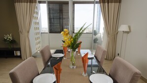 A dining table set for six with chairs, a vase with flowers, and a view of the city through large windows. - The Apartments Dubai World Trade Centre (Dubai)