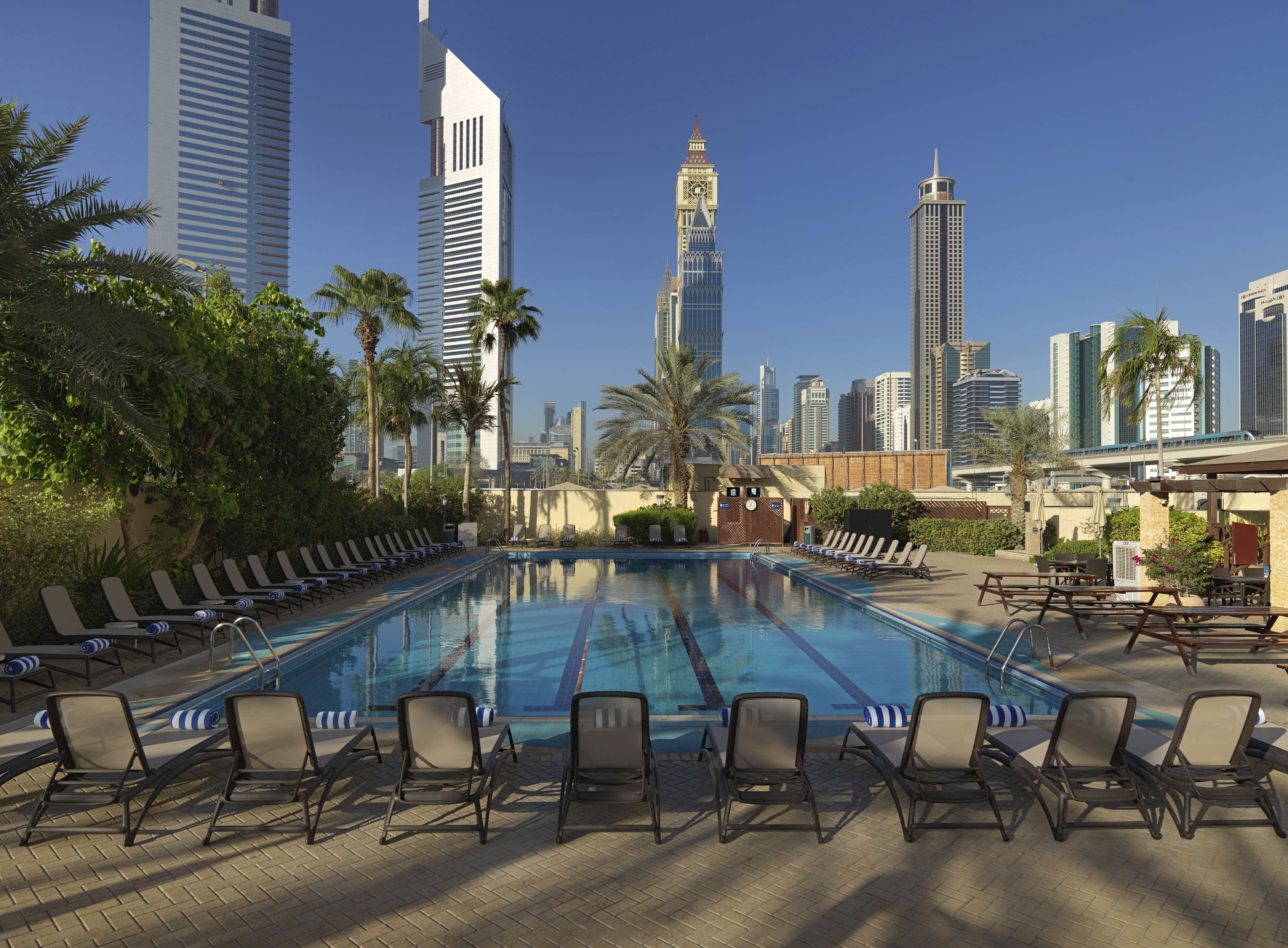 Une piscine entourée de chaises longues et de palmiers, le tout bordé d’immeubles imposants.