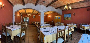 Un restaurante con varias mesas y sillas, arcos de ladrillo y suelo de baldosas.