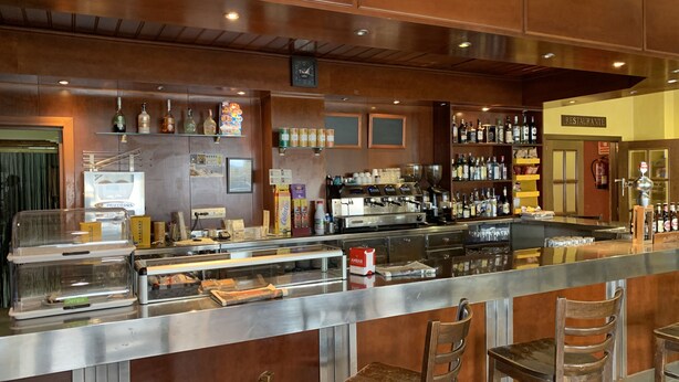 A bar area with a counter, stools, and shelves stocked with bottles. - Hostal Monasterio de Rueda (Sastago)