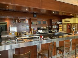 Una zona de bar con mostrador, taburetes y estanterías llenas de botellas.