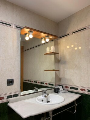 A bathroom with a white sink, a mirror, and a shelf with toiletries.