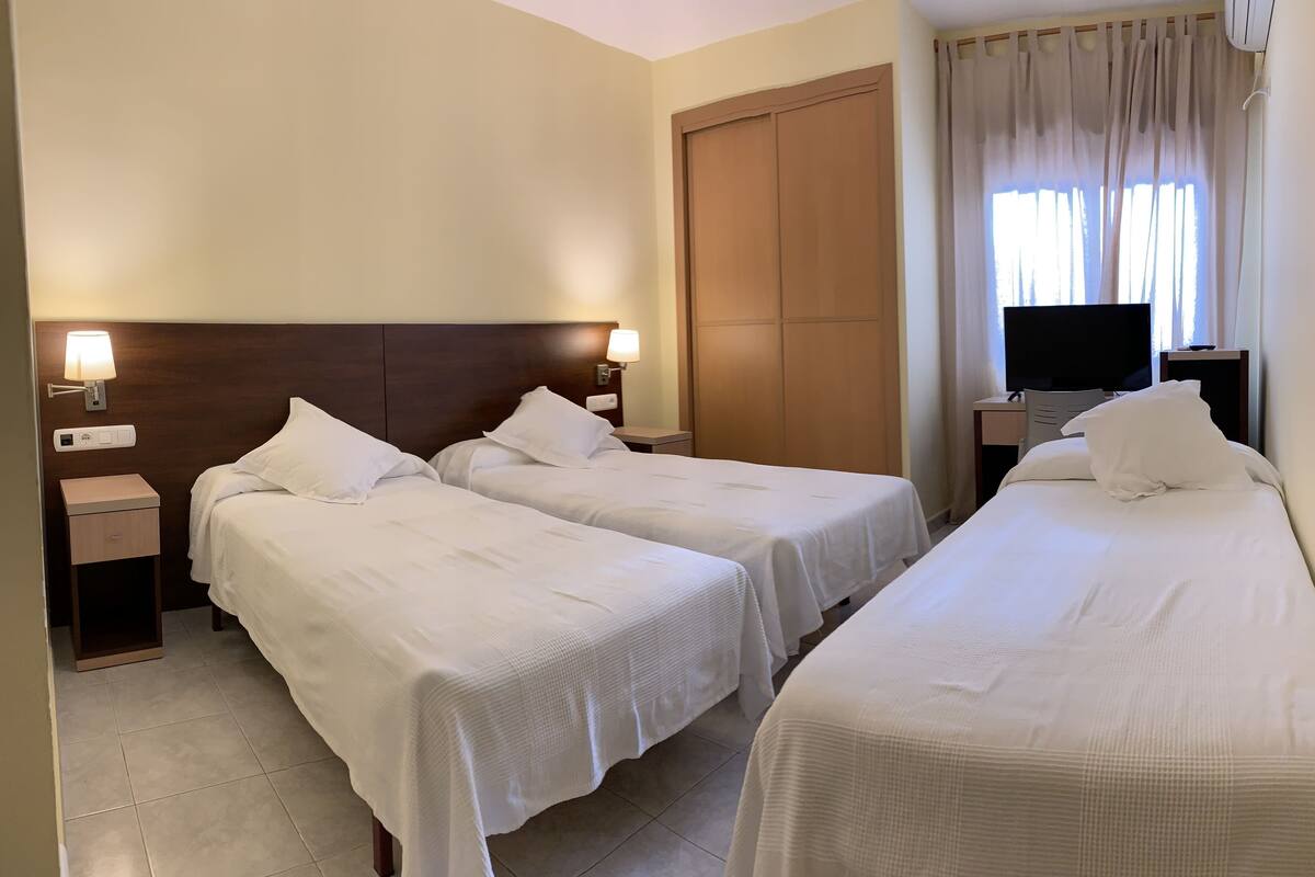A hotel room with two single beds, a desk with a TV, and a wardrobe.