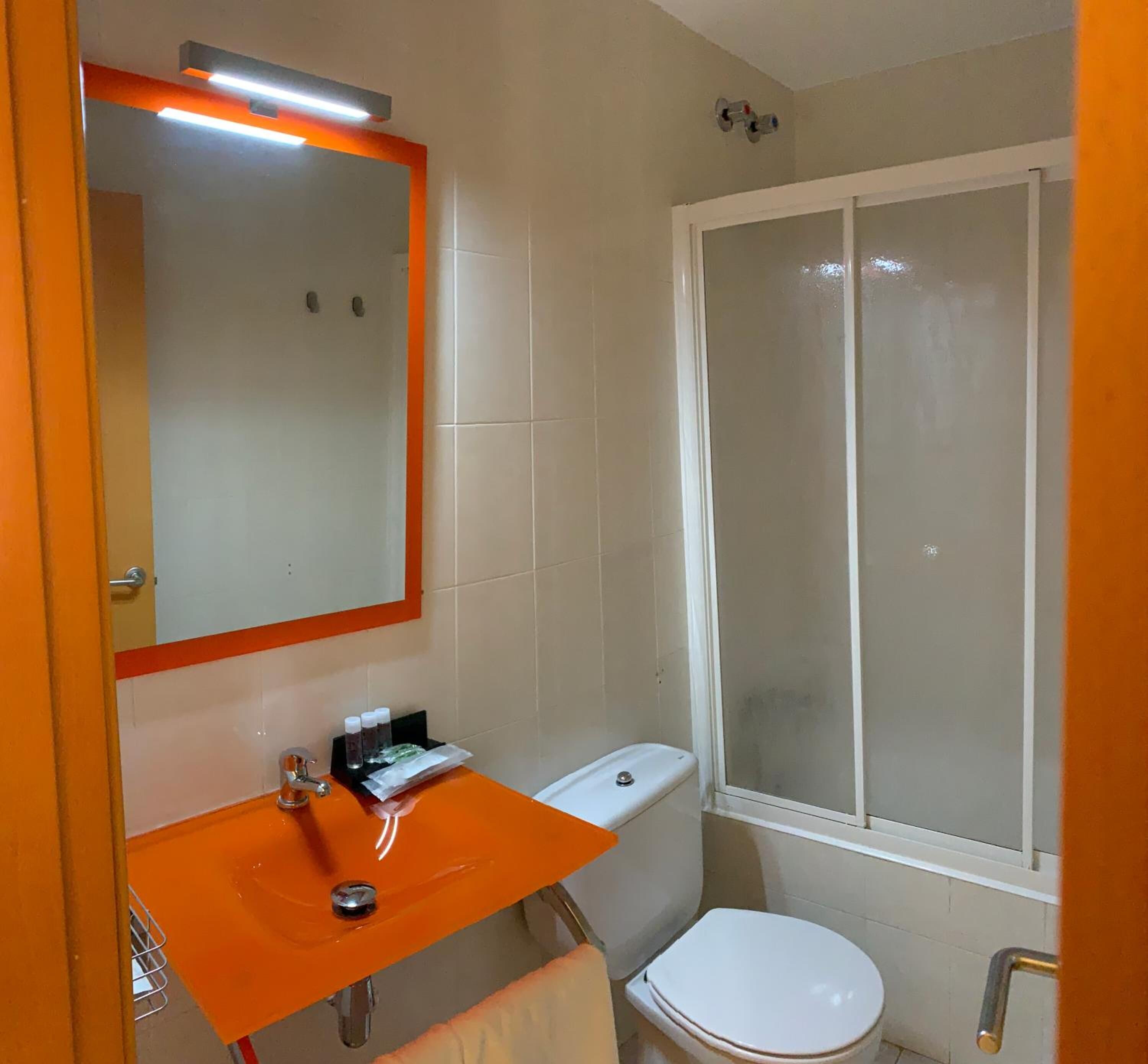 A bathroom with a white toilet, an orange sink, a mirror, and a shower with a frosted glass door.