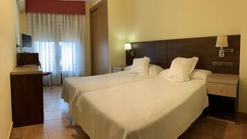 A hotel room with two beds, a desk with a computer, a TV, and a window with curtains.