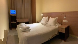 A hotel room with a bed, pillows, a nightstand, a TV, and a bathroom area with a towel rack. - Hostal Monasterio de Rueda (Sastago)