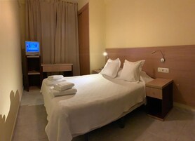 Habitación de hotel con cama, almohadas, mesita de noche, televisión y zona de baño con perchero.