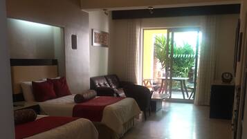 Habitación de hotel con dos camas, un sofá, un comedor con mesa y sillas, y un ventanal corredero que da a un espacio exterior.