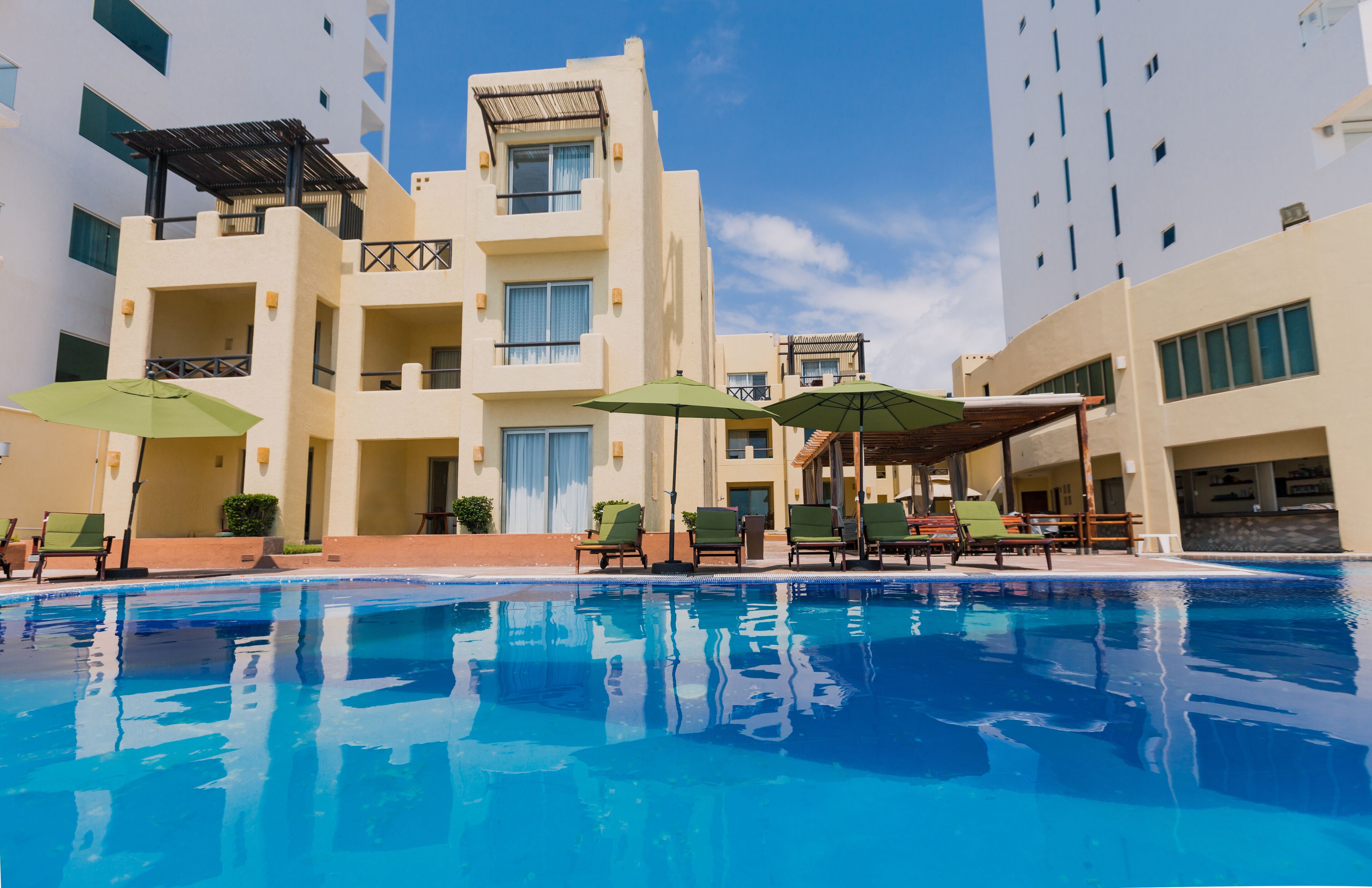 A swimming pool with lounge chairs and umbrellas, surrounded by multi-story buildings with balconies and windows.
