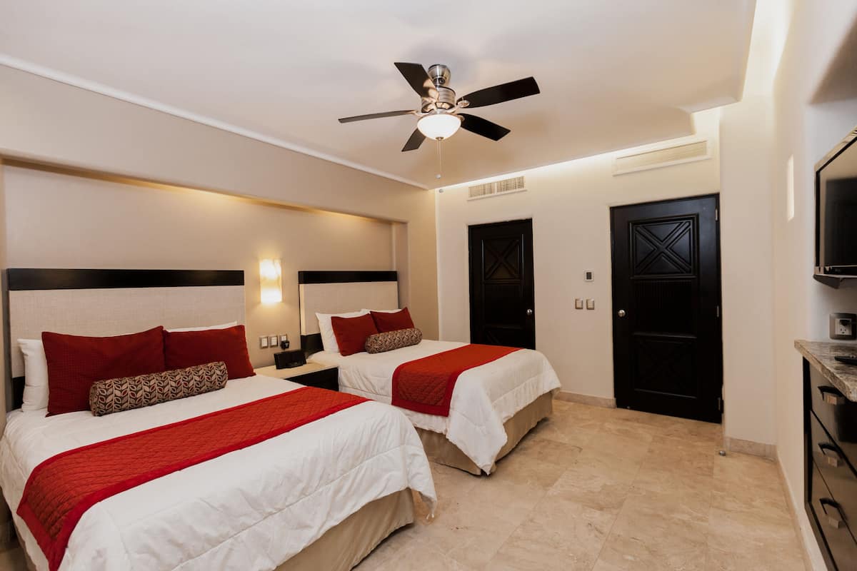 Habitación de hotel con dos camas, ventilador de techo, televisor y puerta con manija negra.
