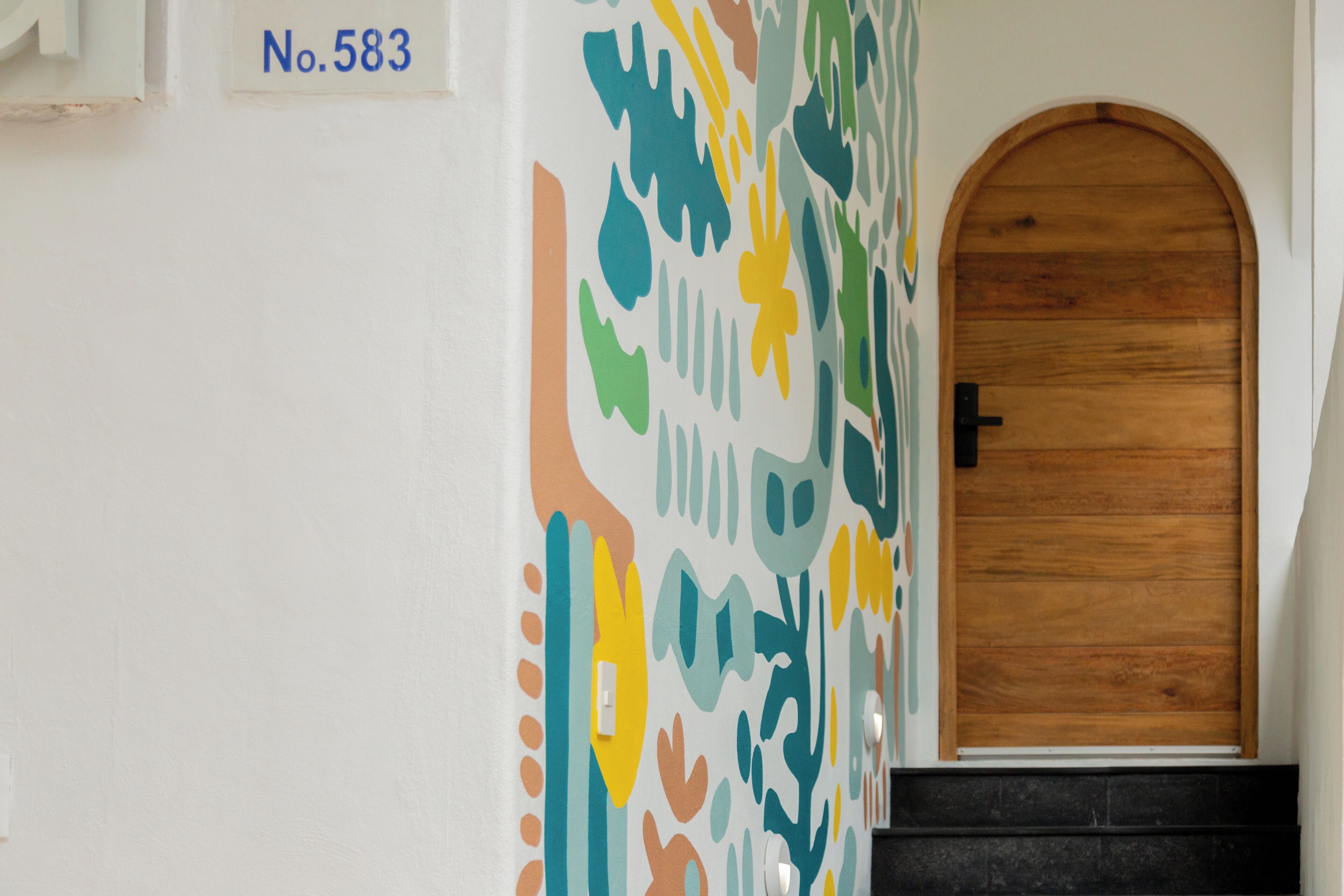 A hallway with a wooden door and a wall with a colorful abstract pattern.
