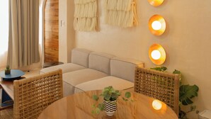 A modern living room with a round wooden table, wicker chairs, a ceiling fan, and wall-mounted lights. - Hotel Amaca Puerto Vallarta - Adults Only (Puerto Vallarta)