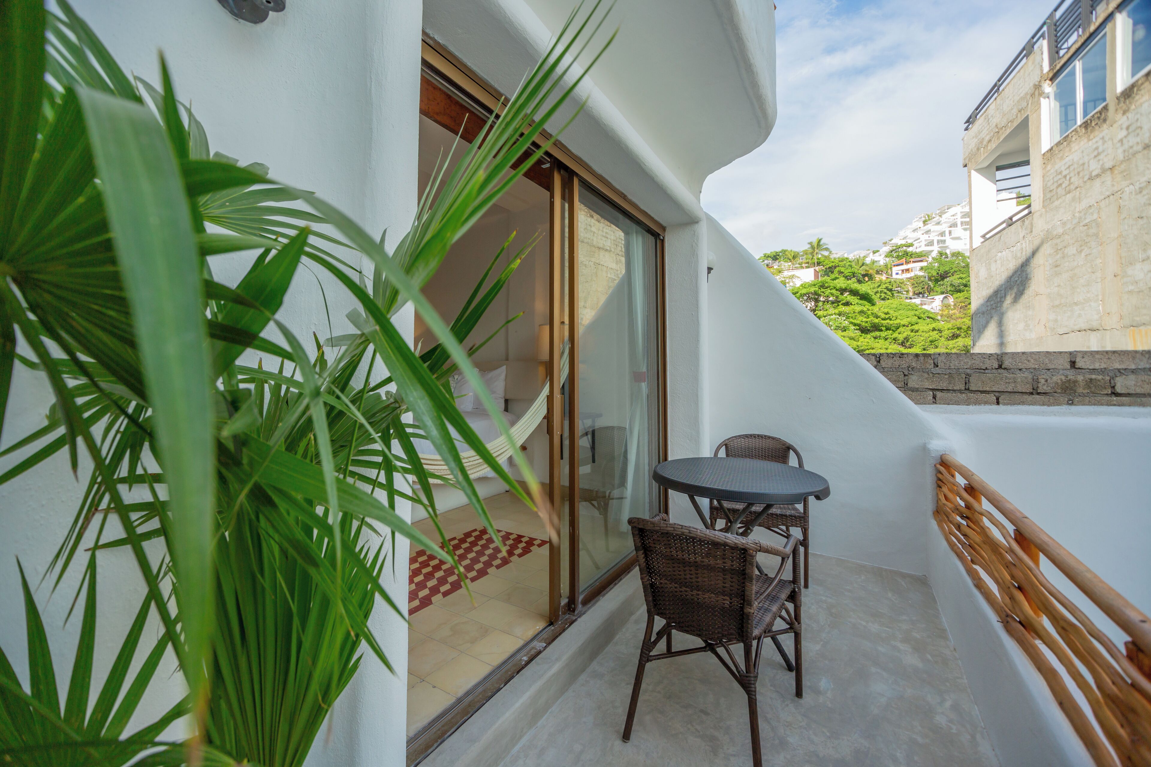 Un balcon avec une table et des chaises, une porte vitrée et une vue sur un immeuble et de la verdure.