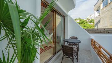 Un balcon avec une table et des chaises, une porte vitrée et une vue sur un immeuble et de la verdure.