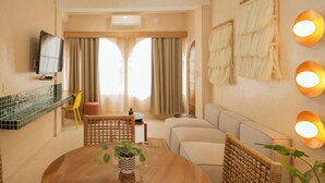 A modern living room with a sofa, a dining table with a plant, a TV mounted on the wall, and a kitchen area with a counter and chairs. - Hotel Amaca Puerto Vallarta - Adults Only (Puerto Vallarta)