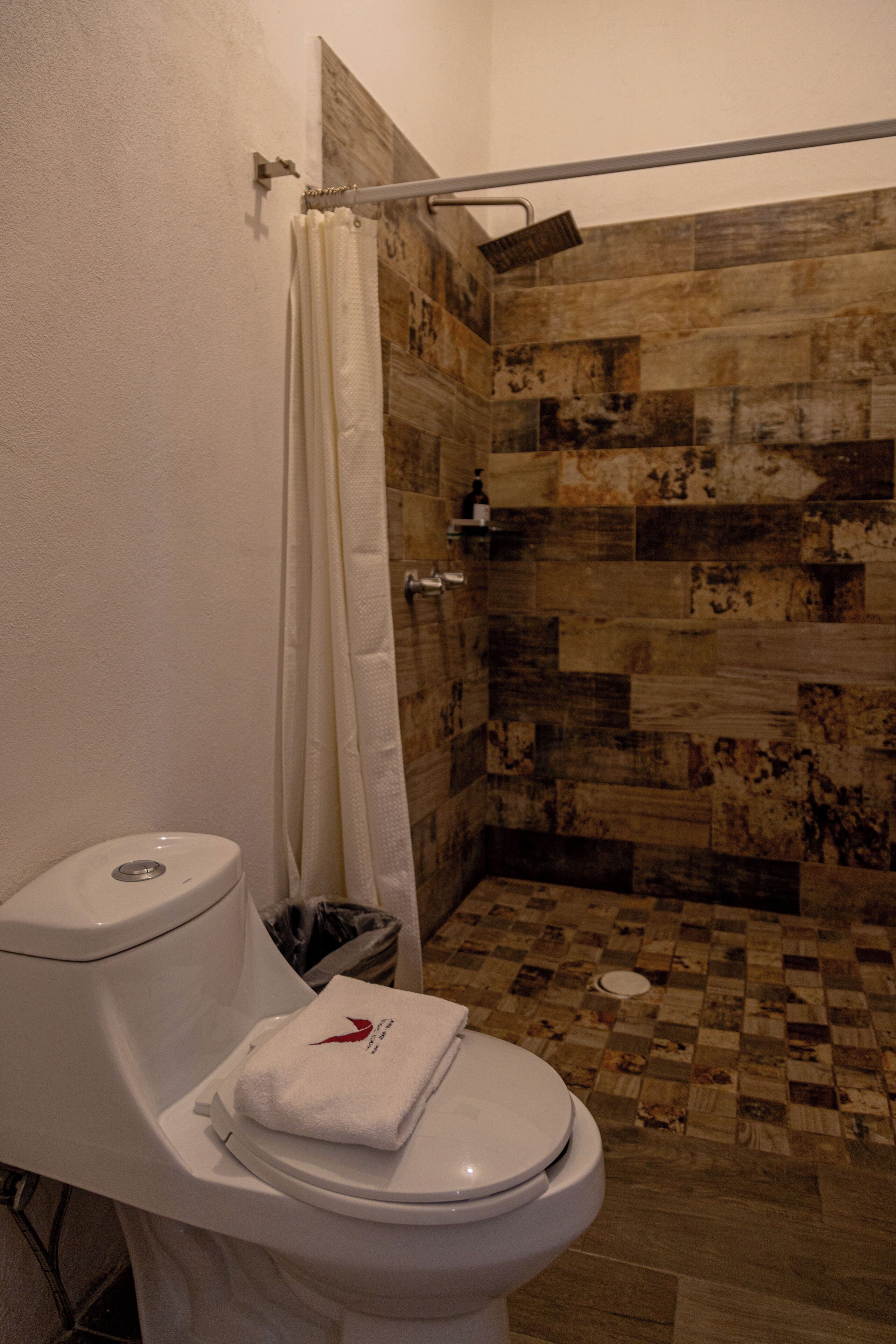 A bathroom with a shower, a toilet, and a towel on the toilet.