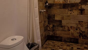 A bathroom with a shower, a toilet, and a towel on the toilet.