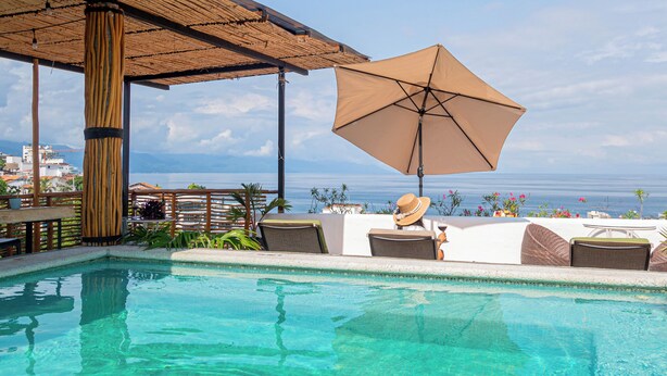 A clear blue pool with lounge chairs and an umbrella, overlooking a body of water. - Hotel Amaca Puerto Vallarta - Adults Only (Puerto Vallarta)