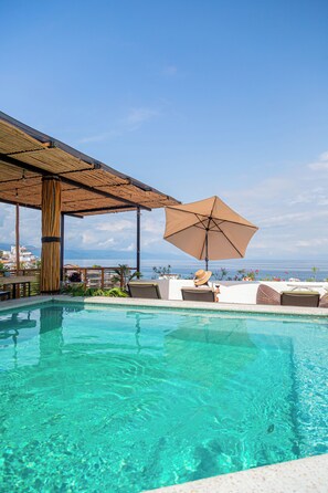 Una piscina azul cristalina con sillas de descanso y una sombrilla, con vistas a una extensión de agua.