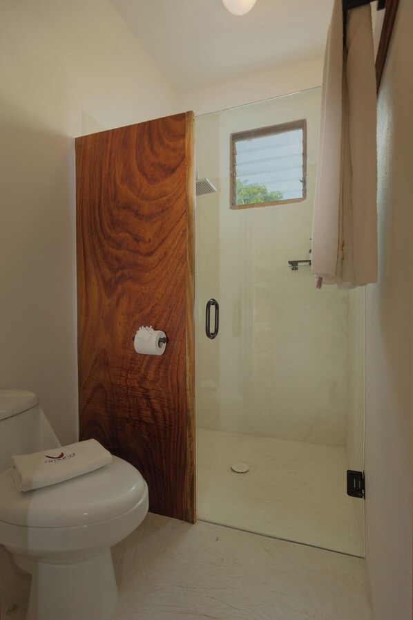 Un baño con puerta de madera, cabina de ducha de vidrio y un inodoro con una toalla encima.