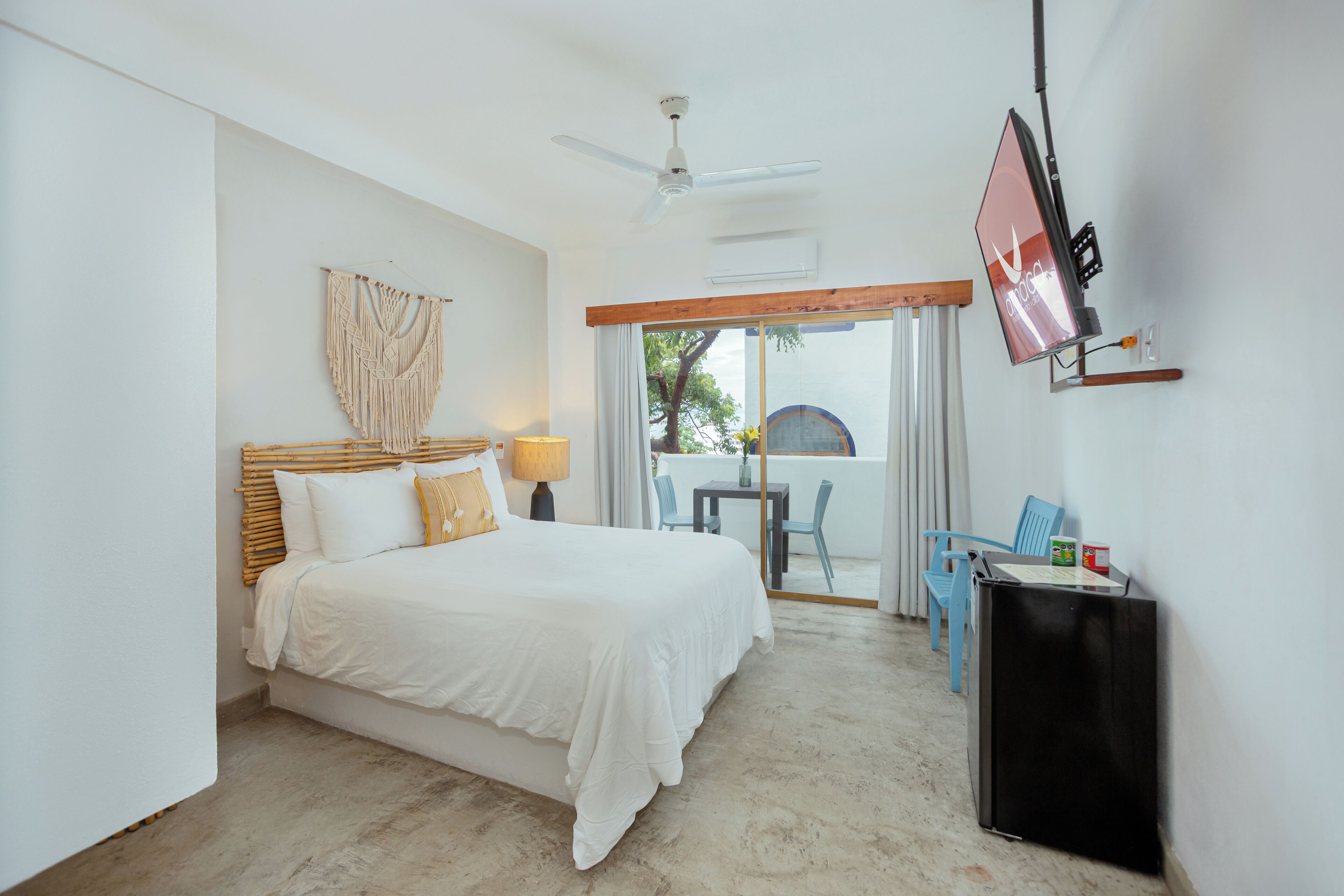 A bedroom with a bed, a ceiling fan, a TV, and a balcony with chairs.