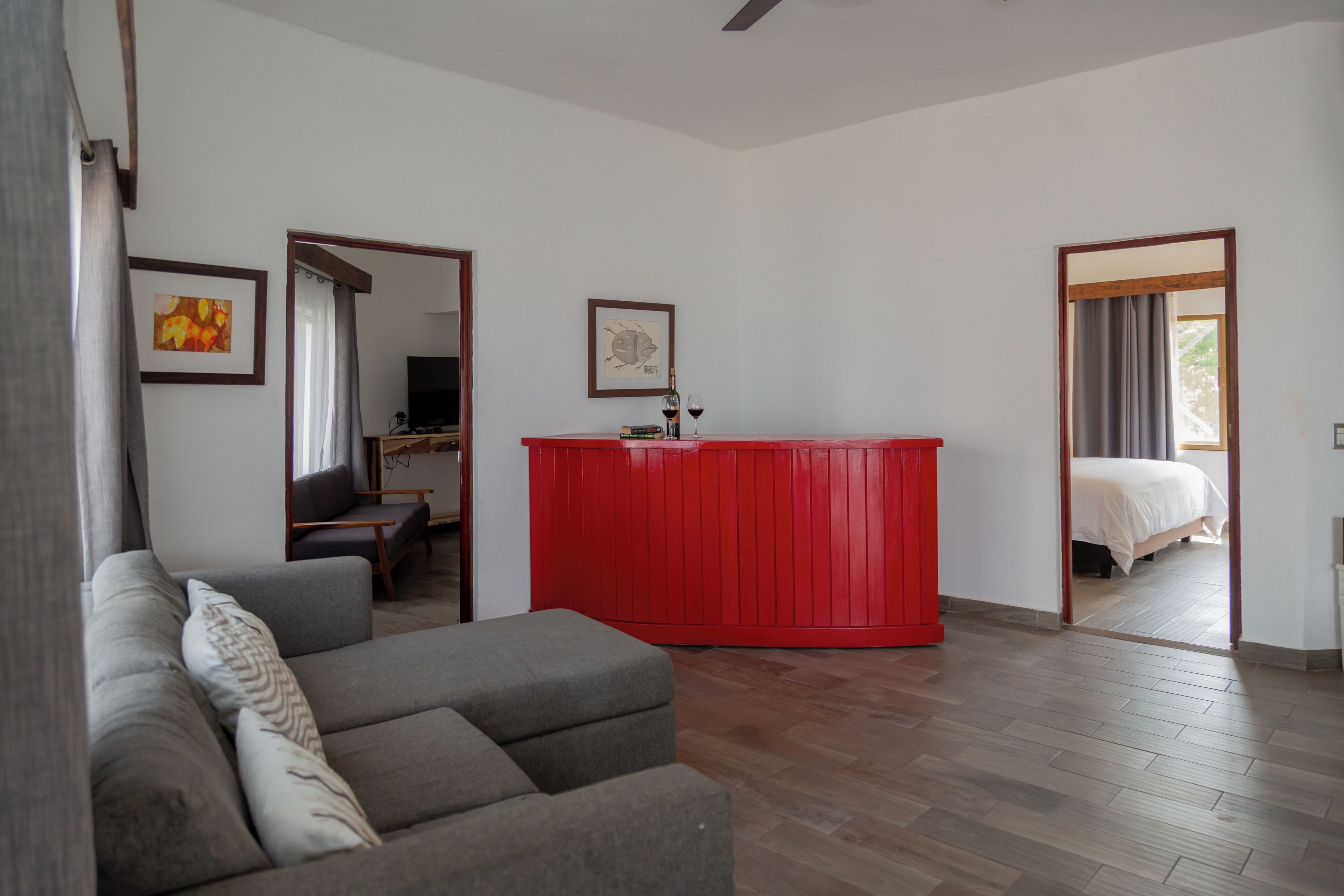 Una sala moderna con un sofá gris, una pared de acento roja y piso de madera.