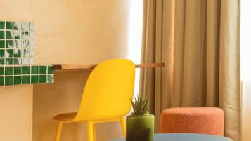 Um quarto com uma mesa redonda, uma cadeira amarela, um espelho redondo, uma planta verde e um banquinho vermelho.