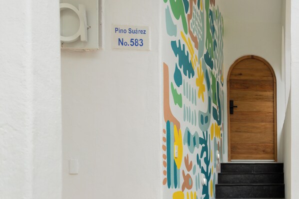 Un pasillo con una puerta de madera y un diseño abstracto y colorido en la pared. Un cartel sobre la puerta dice 'Pino Suárez No. 583'.