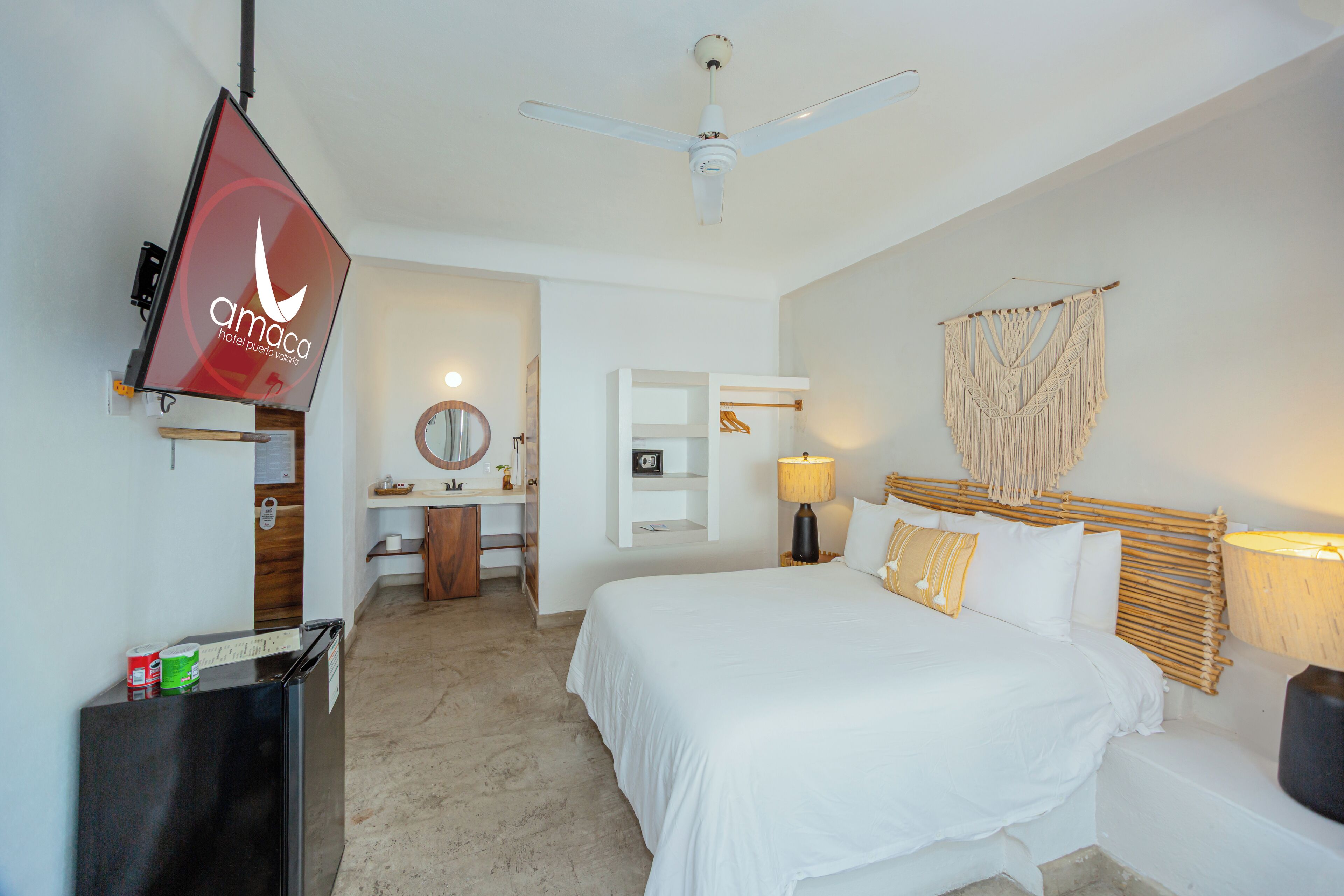 Une chambre d’hôtel comprenant un lit, un bureau avec une chaise, un miroir, un téléviseur fixé au mur et un ventilateur de plafond.