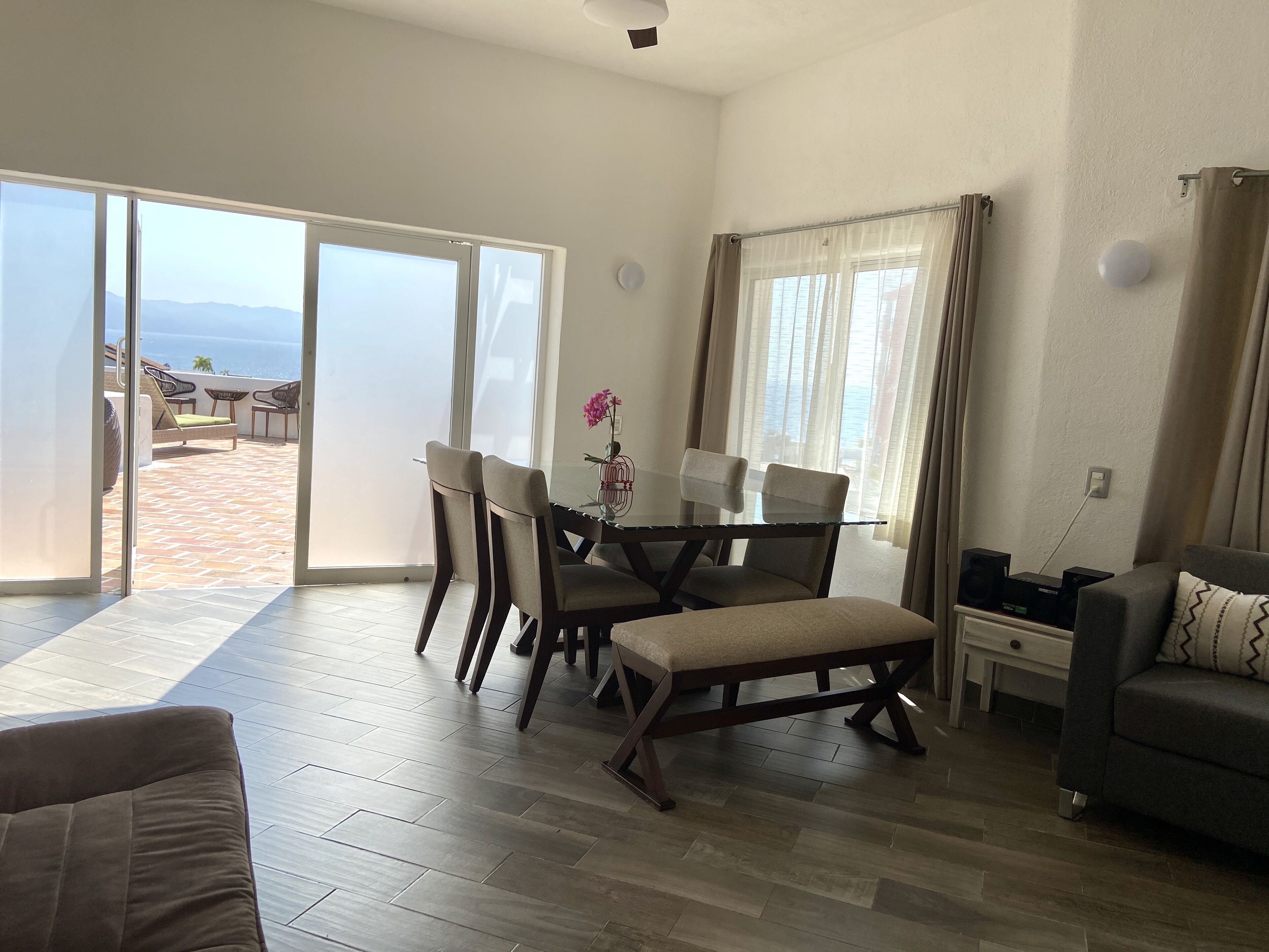 Un vaste espace de vie comprenant une table à manger, des chaises, un canapé et une vue sur la mer grâce à de grandes portes coulissantes.
