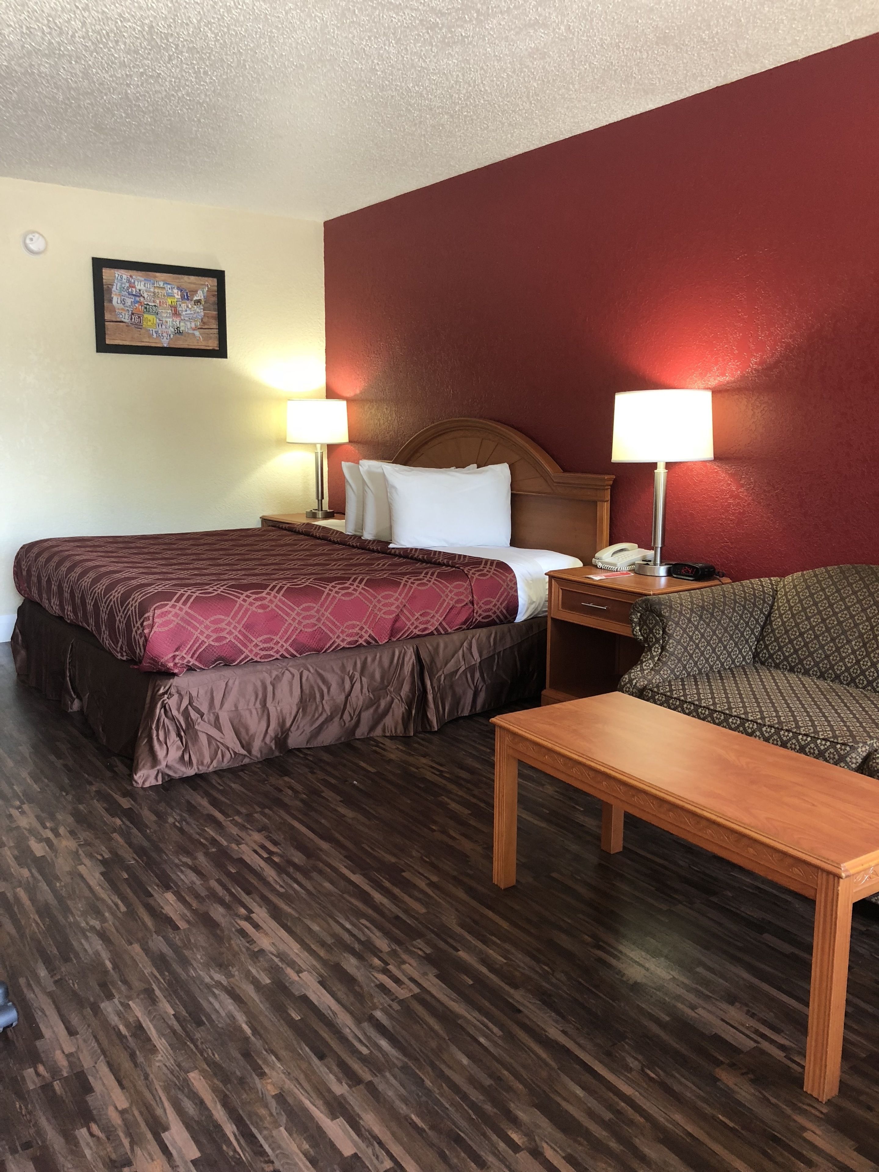 A hotel room with a bed, a sofa, a wooden table, and a nightstand with a lamp.