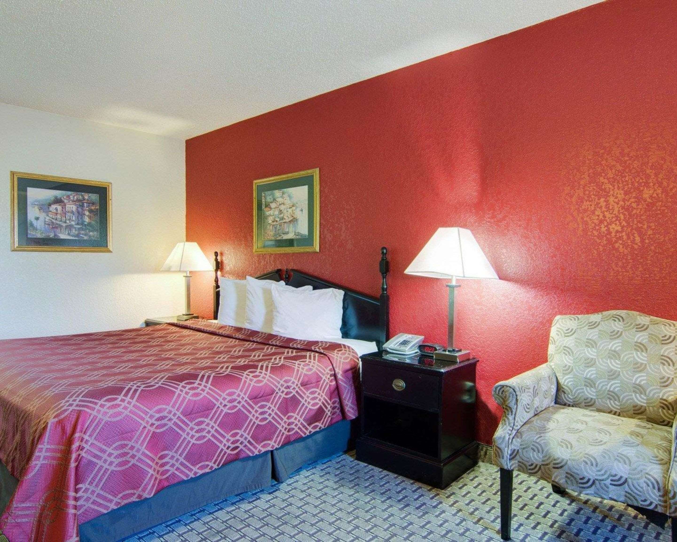 Una habitación de hotel con una cama, dos mesitas de noche, una silla y dos lámparas fijadas a la pared.