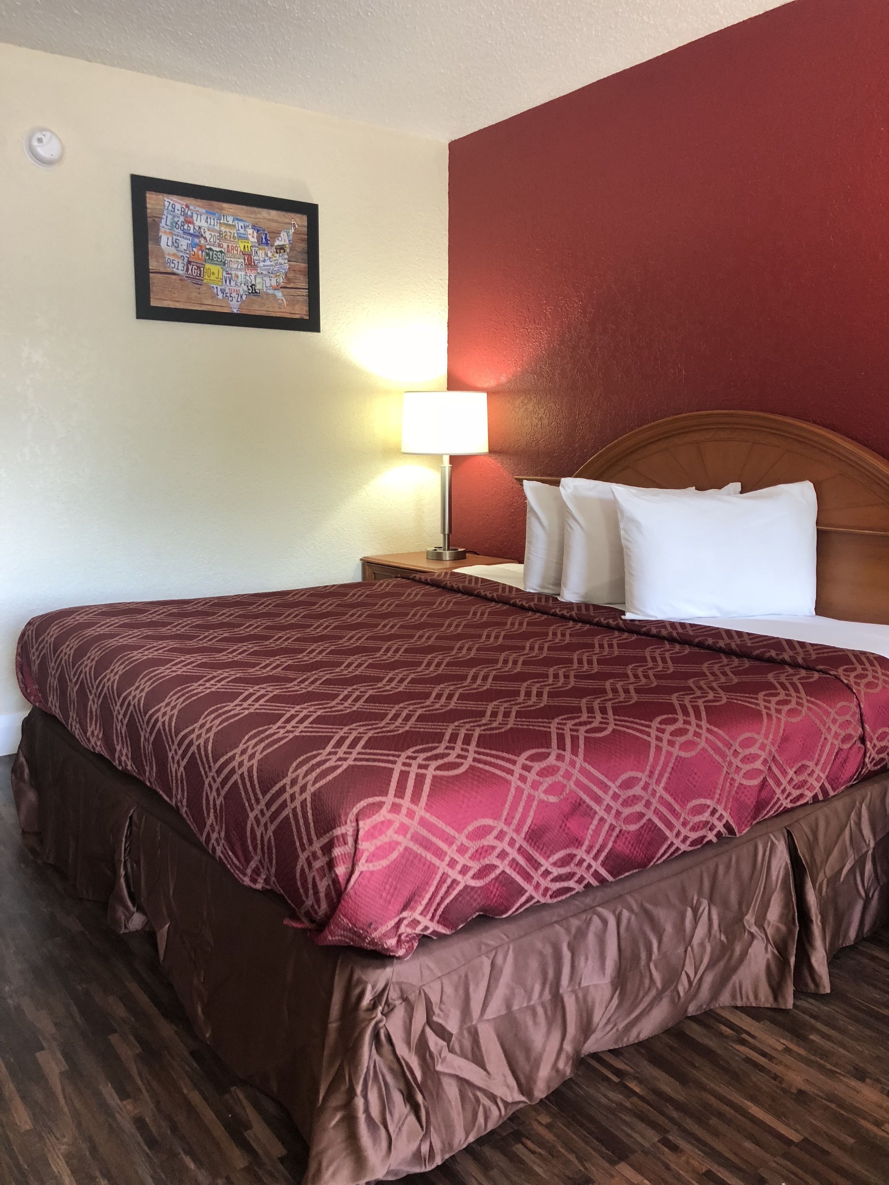 A hotel room with a large bed, a wooden headboard, a nightstand with a lamp, and a wall map.