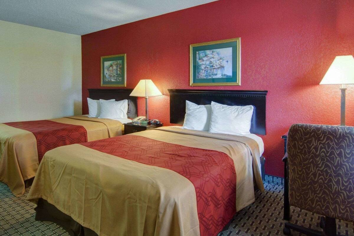 A hotel room with two beds, red walls, and two paintings.